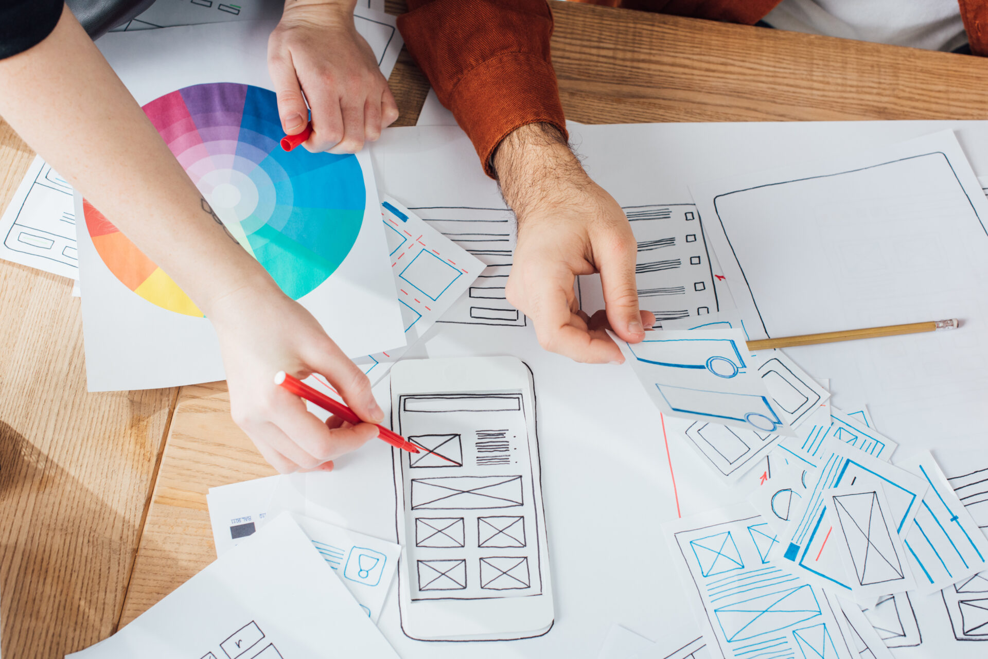 Cropped view of designers planning user experience design with layouts and color circle on table