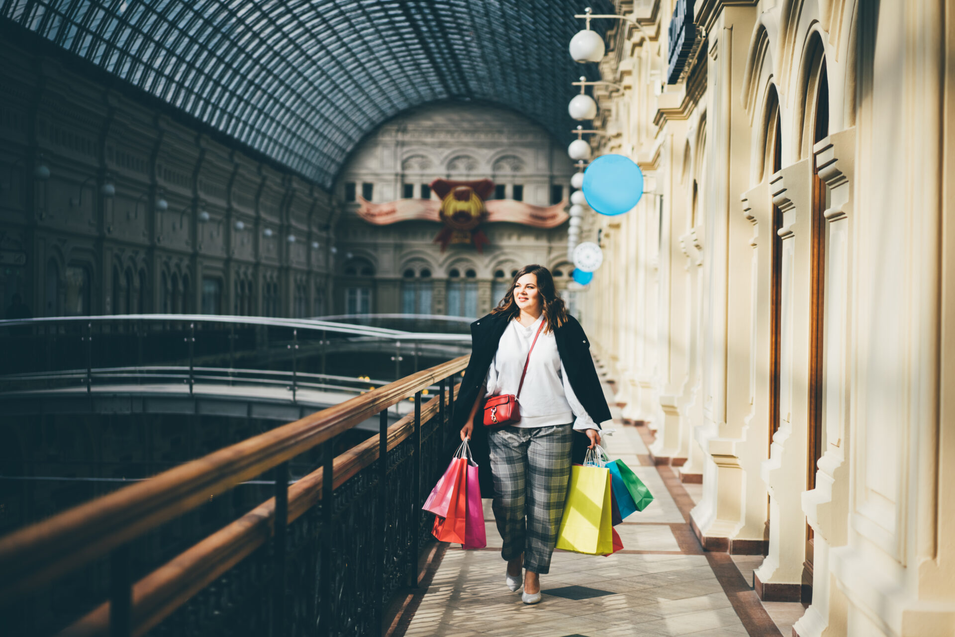 Happy young woman in casual clothing with shopping bags, at shopping mall. Plus size model in sales, shop, retail. Portrait of a&nbsp;happy girl after a&nbsp;successful purchase.